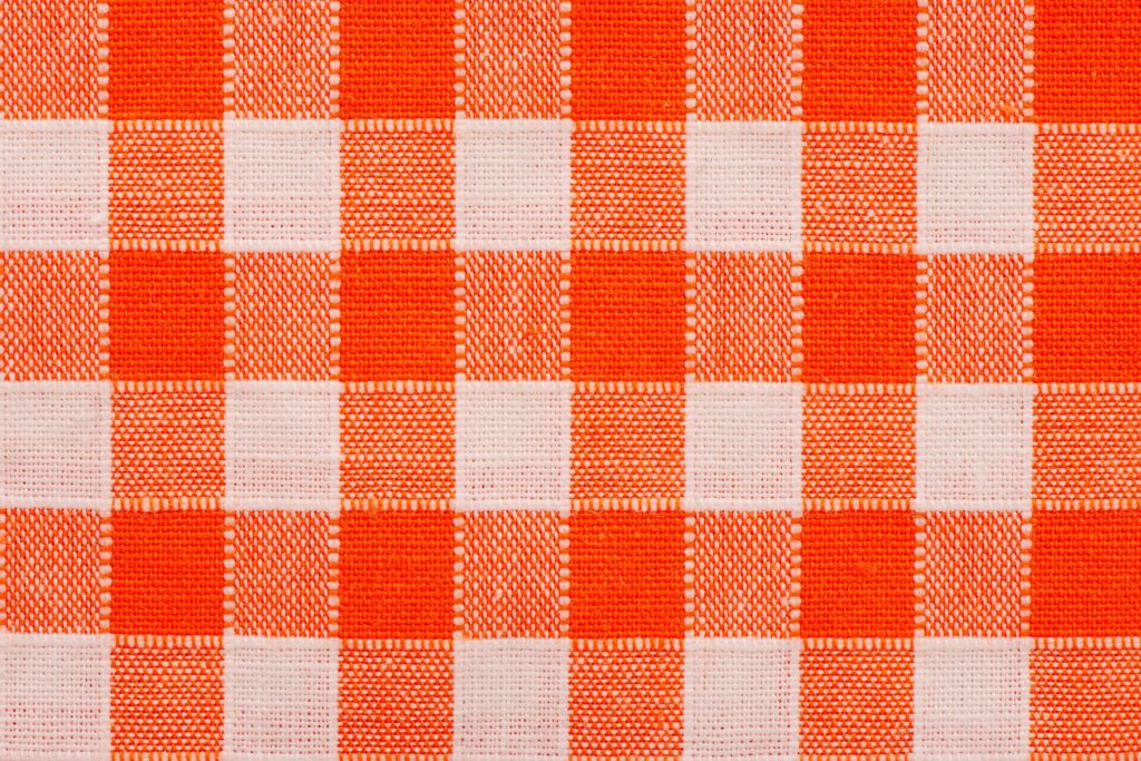 Close-up of orange and white gingham checkered fabric with a rustic woven texture.