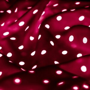 Lush deep red fabric with white polka dots, flowing curves and soft waves forming a rich texture background